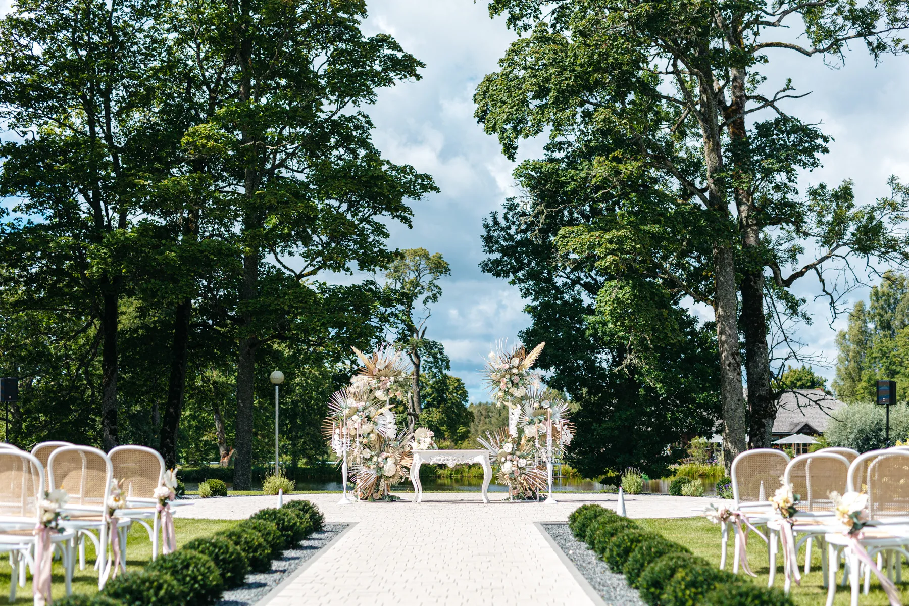 Ort der Hochzeitszeremonie im Park von Igates pils mit weißen Stühlen und Blumenbogen